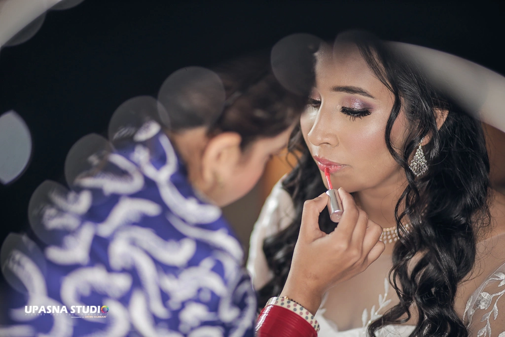 A bride getting her makeup done by a woman at Upasna Studio, a wedding photographer and candid wedding photographer.
