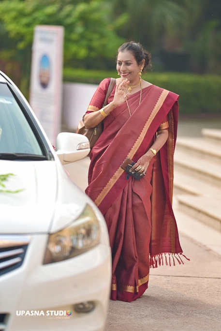 Upasna studio | Wedding photographer in delhi | A woman in a red sari standing next to a car, showcasing vibrant cultural attire and a stylish vehicle.