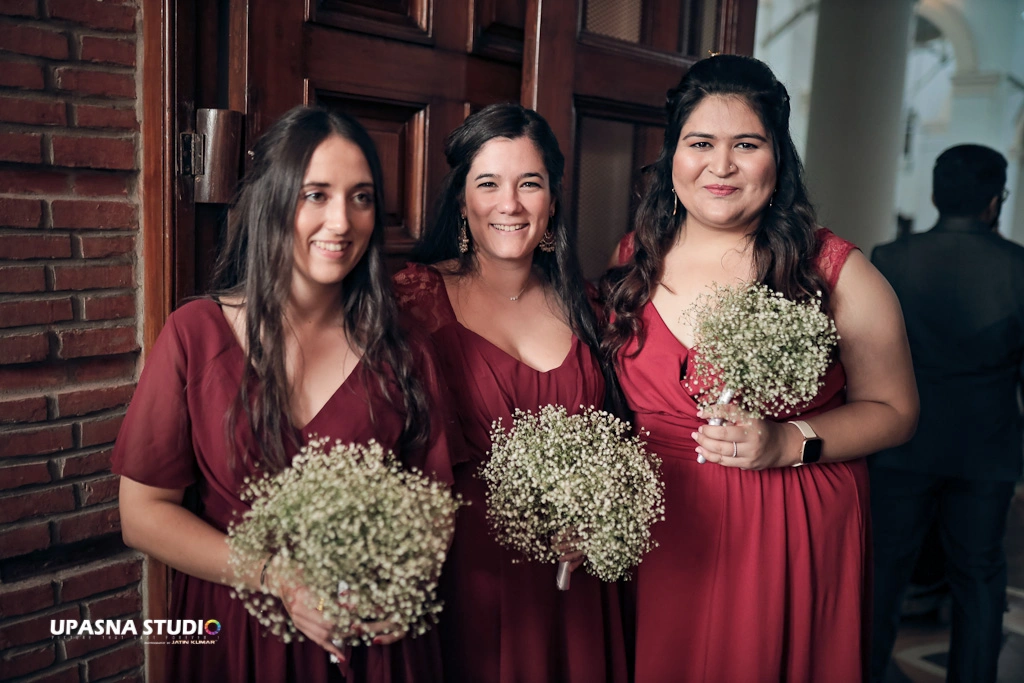 Wedding Photographers in Delhi | Upasna Studio | Three bridesmaids in red dresses holding bouquets.